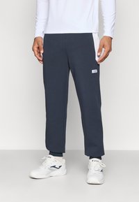 Mørkeblå treningsbukser med innsvingt snitt, elastisk midjebånd og sidemeshpaneler. Kombinert med hvite joggesko.