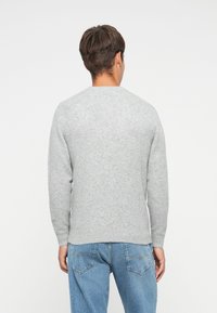 Gray knitted sweater with long sleeves and a round neckline, featuring a smooth texture. Worn with light blue denim jeans.