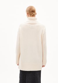 Beige wollen turtleneck sweater met een ontspannen pasvorm, geribbelde manchetten en zoom, met een klein vierkant detail op de achterkant.