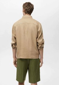 Tan linnen skjorte med oprullede ærmer, rygstykke og lige kant, parret med grønne shorts med en tekstureret overflade og bred pasform.