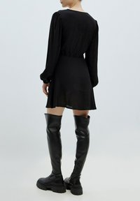 Zwart lange mouw jurk met een getailleerde taille en een vloeiende rok. Draag het met zwarte leren laarzen tot boven de dij met een dikke zool.