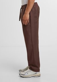 Bruine joggers van een katoenmix met een elastische tailleband, zijzakken en een taps toelopend ontwerp, gecombineerd met grijze en zilveren sportschoenen.