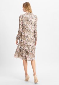 Blumendruckkleid mit langen Ärmeln, einem Rüschensaum und einem leichten Stoff. Die Farben umfassen Rosa, Grün und Braun mit dezenten Mustern.