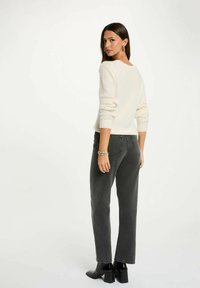 Maglione lavorato a maglia color avorio con scollo a barchetta e polsini a coste, abbinato a jeans grigi scuri a vita alta e stivali neri alla caviglia.