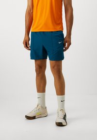 Pánske atletické oblečenie pozostávajúce z oranžového trička s krátkymi rukávmi, tyrkysových šortiek a bielych ponožiek Nike doplnených viacfarebnými topánkami.