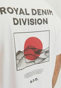 White t-shirt featuring a graphic of red sun and abstract black wave patterns. Text above reads "ROYAL DENIM DIVISION" and below "R.D.D."