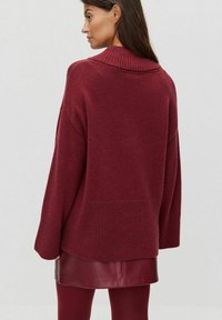 Burgundowy, oversize sweter z prążkowanym kołnierzem i mankietami, o fakturowanym splocie i opadających ramionach, zestawiony z skórzaną spódnicą.
