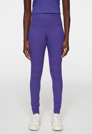 Lila gerippte Leggings mit einem hohen Bund, ausgestattet mit einer glatten Textur. Tragen mit hellen sportlichen Schuhen.