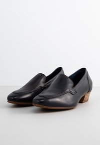 Chaussures noires en cuir à enfiler avec un bout pointu, des détails de couture minimaux et un petit talon empilé pour une apparence raffinée.