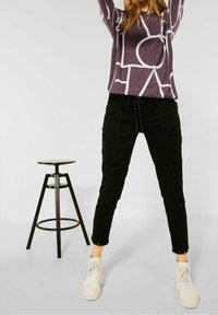 Maglietta lunga viola con motivo astratto bianco, abbinata a pantaloni neri a sigaretta con coulisse. Sneakers alte bianche incluse.