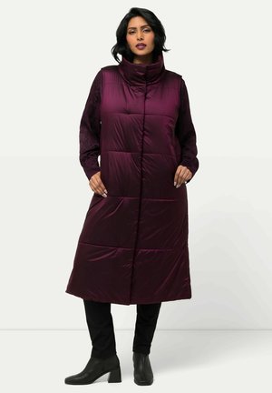 Gilet lungo in piuma di prugna con colletto alto, motivo a rombi e tasche laterali, indossato sopra un top nero a maniche lunghe e pantaloni.