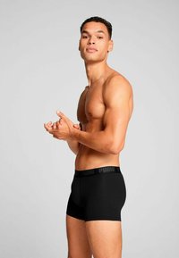 Black boxer shorts with a soft waistband featuring the "PUMA" logo. The fabric is smooth and fitted, outlining a toned physique.