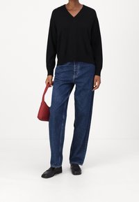 Un pull en tricot noir avec décolleté en V, un jean en denim bleu ample, et un sac à main rouge. Des mocassins noirs complètent la tenue.