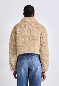 Beige fluffy kort jakke med krage og oversized ermer, kombinert med blå høytaljede jeans med baklommer.