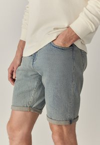 Lichtblauwe denim_short met opgerolde zomen, met een klassieke pasvorm en subtiele structuur. De stof heeft een vervaagde uitstraling die typerend is voor denim.