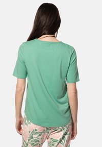 Korte mouwen, ronde hals T-shirt van lichtgroene stof, gecombineerd met een broek met een patroon in roze en groene bloemenontwerpen.