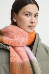 Fular tricotat, cu nuanțe vibrante de portocalie, roz și verde. Are o textură moale și este înfășurat în jurul gâtului, peste o jachetă gri.