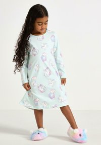 Hellblaues Nachthemd mit langen Ärmeln, das ein verspieltes Einhorn- und Wolkendesign zeigt; kombiniert mit bunten, flauschigen Hausschuhen.