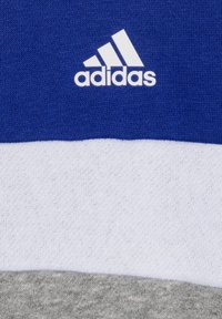 Ropa deportiva Adidas con una sección superior azul, parte media blanca y parte inferior gris, fabricada en un tejido suave con un acabado texturizado.