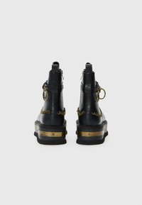 Boots negri din piele pentru gleznă, cu o talpă groasă, accente din lanț aurit și un detaliu metalic pe toc. Prezintă un design cu elemente metalice în formă de bucle.