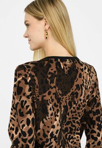 Maglietta a maniche lunghe con stampa leopardata, caratterizzata da tonalità di marrone e nero. Collo rotondo con un piccolo dettaglio del logo dorato sul retro. Tessuto morbido.