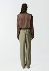 Smeđi satenasti košulja dugih rukava i široke hlače na karirane uzorke u zelenoj boji, s elastičnom jablanom i dva stražnja džepa. Glatka tekstura, opušteni kroj.