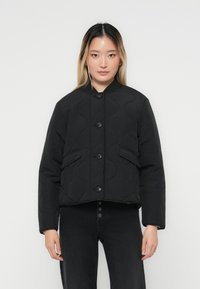 Veste matelassée noire avec un col rond, fermée par des boutons à l'avant et dotée de deux poches latérales. Elle présente un design court et une texture lisse.