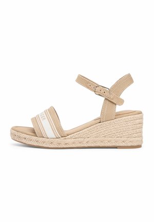 Beżowy sandał na klinie z paskiem wokół kostki, zapinany na klamrę, z plecioną podeszwą w stylu espadryli oraz przednim paskiem z białej tkaniny z subtelnym detalem tekstowym.