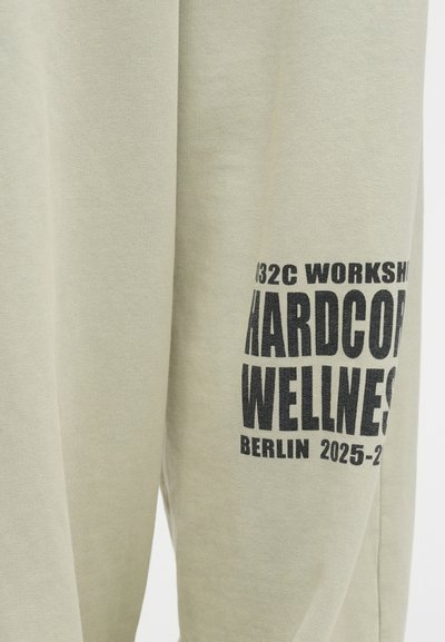 Jasnozielony sweatshirt wykonany z bawełny, z wyraźnym czarnym nadrukiem. Tekst obejmuje "032C WORKSHOP HARDCORE WELLNESS BERLIN 2025-2026."