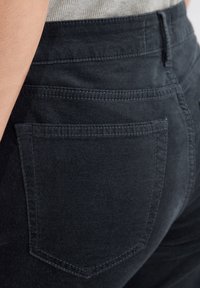 Zwarte katoenen broeken hebben een soepele textuur, achterzakken met stiksels en een getailleerd design rond de taille en heupen.