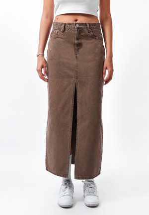 Bruine denim maxi rok met een hoge taille en een front split, afgewerkt met contrasterende stiksels. Gdrag met witte sneakers en enkelkousen.