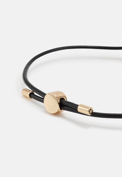 Black leather cord necklace featuring a circular gold clasp and two gold accents at the ends. Smooth texture with a minimalist design.