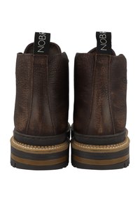 Hnědé kožené kotníkové boty s texturovaným povrchem, béžovým prošíváním a gumovou podrážkou. Mají poutko pro snadné nazouvání a zaoblený design na zadní straně.