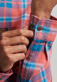 Red and blue plaid flannel shirt, featuring button closures on the cuffs. The fabric appears soft with a visible texture and pattern.