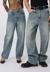 Jeans azul claro de corte relajado, con cintura alta, un ligero desgaste y costuras detalladas. Combinados con un cinturón negro y calzado de contraste.