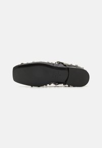 Suela de zapato de cuero negro con una textura suave. Presenta tachuelas plateadas a lo largo del costado y un pequeño tacón cuadrado. Logo de la marca estampado visible.