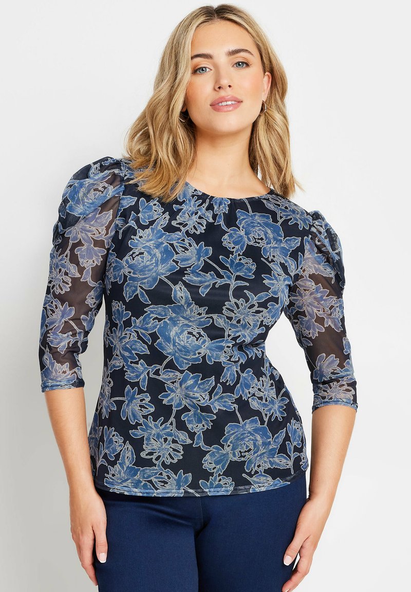 Blusa floreale blu con maniche trasparenti, caratterizzata da un collo rotondo e spalle a sbuffo. Il motivo presenta fiori blu chiari su uno sfondo scuro.