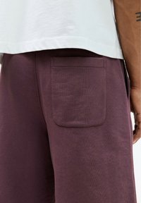 Shorts en coton violet avec une poche plaquée à l'arrière. Les shorts ont une texture douce et sont associés à une chemise blanche à coupe décontractée.