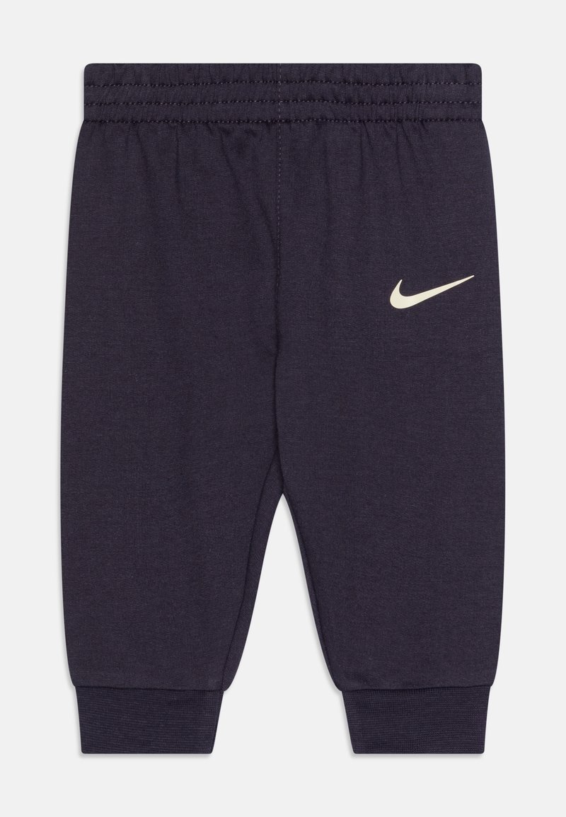 Granatowe dżinsowe spodnie dresowe z elastycznym pasem i ściągaczami na kostkach, z małym kremowym logo Nike na lewym nogawce.