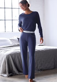 Tumedate loungewear komplekt, mis sisaldab pikki varrukaid ja sirget lõikega pükse, valmistatud pehmest kangast, millel on valge bränditud elastne vöökoht.