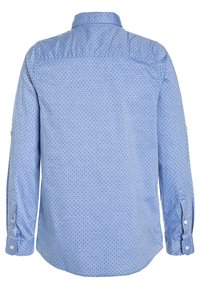 Camisa de manga larga de color azul claro con cuello abotonado, que presenta pequeños lunares marinos y puños de un solo botón. Textura de tela suave.