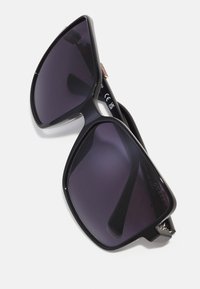 Black oversized sunglasses with dark gradient lenses, a smooth plastic frame, and metal accents at the temples. Logo visible on the side.