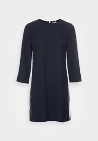Navyblaues Kleid mit Dreiviertelärmeln, Rundhalsausschnitt, seitlichen Schlitzen und kontrastierenden weißen und roten Streifen entlang der Seiten. Glatte Stoffoberfläche.