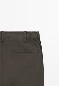 Dunkelgraue Hose mit elastischem Bund, Gürtelschlaufen und einer einzigen Paspeltasche auf der Rückseite rechts.