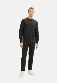 Čierna pletená mikina s okrúhlym výstrihom a dlhými rukávmi, v kombinácii s čiernymi nohavicami úzkeho strihu a bielymi teniskami. Jednoduchý a moderný dizajn.