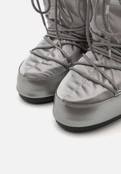 Bottes grises rembourrées avec une finition brillante, mettant en avant des lacets gris complexes et une semelle noire texturée. Design de bout lisse et arrondi.