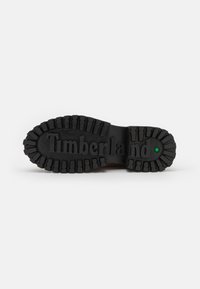 Suola di stivaletto nera in gomma con motivo di battistrada testurizzato. "Timberland" impresso al centro, punto verde accentato sul tallone. Design piatto e robusto.
