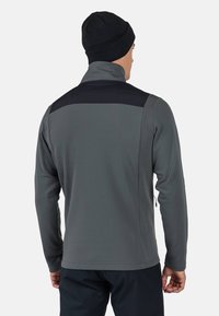 Grå fleecejacka med hög krage, med en svart axelpanel. Långa ärmar och dragkedjefickor på sidorna. Slät textur.