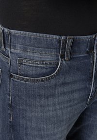 Dunkelblaue Denim-Jeans mit klassischem Schnitt, gestickten Details und mehreren Taschen, mit einer glatten Textur und Metallakzenten.