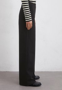 Zwarte wijde broek van gladde stof, met een hoge taille. Gecombineerd met zwarte platte schoenen en een gestreept langslavenshirt.